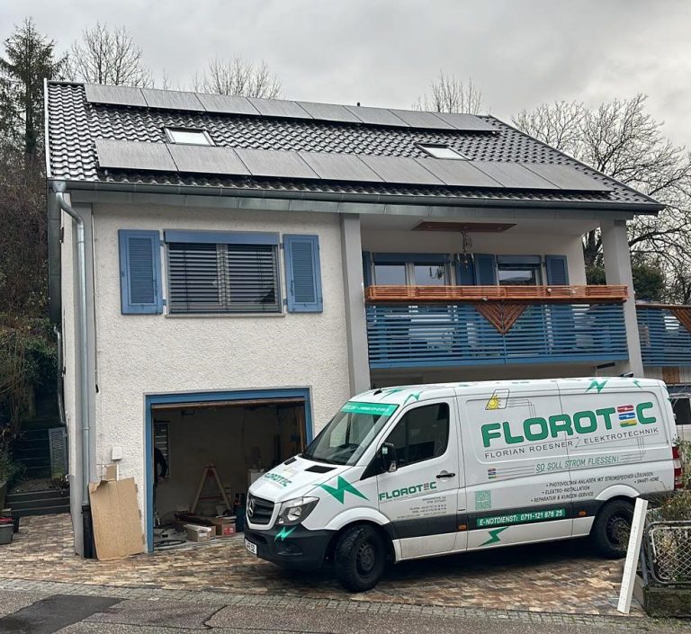 Ein Haus mit blauer Tür, Solarpaneele auf dem Dach und ein Lieferwagen davor