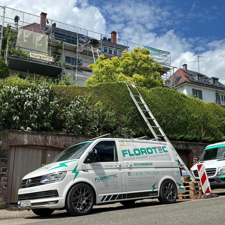 Ein weißer Lieferwagen mit Firmenbeschriftung steht vor einem Haus mit Gerüst.