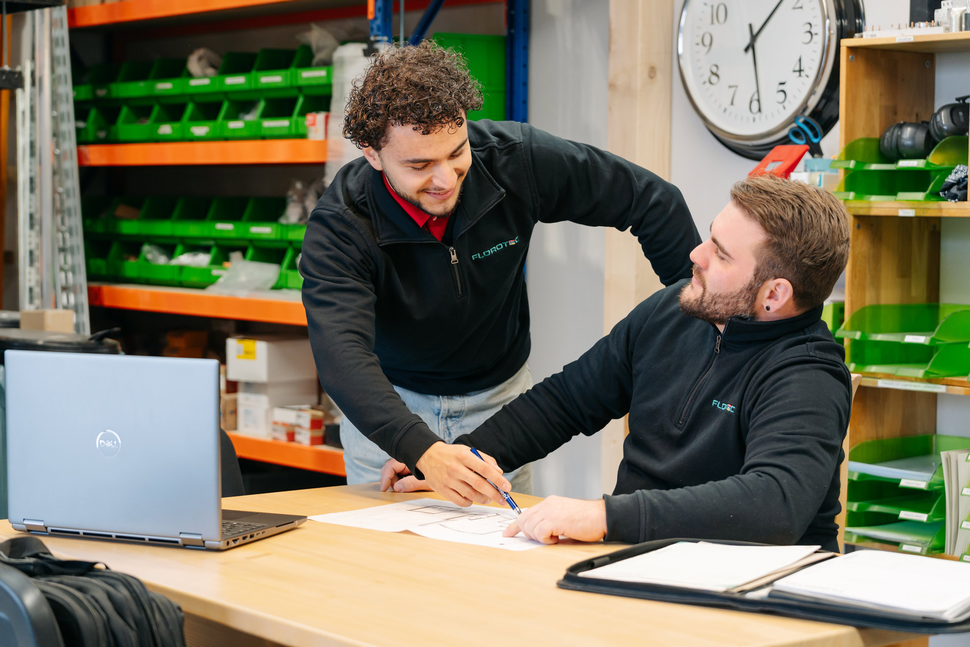 Zwei Männer besprechen freundlich technische Zeichnungen an einem Holztisch im Büro