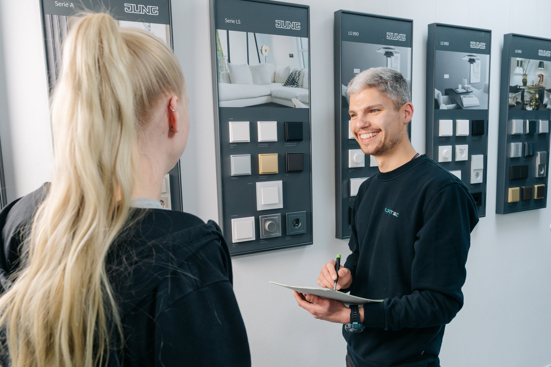 Zwei Personen sprechen freundlich vor einer Wand mit Musterschaltern und Farbtafeln