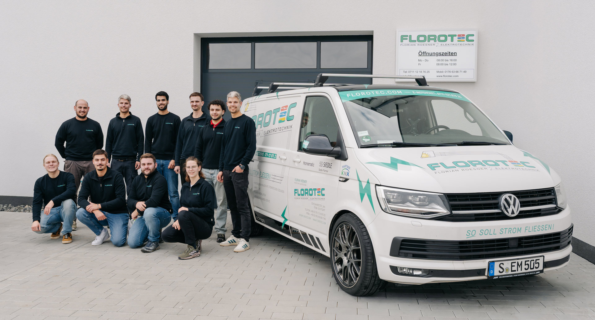 Neun Männer und zwei Frauen lächeln vor einem weißen Firmenwagen und Gebäude