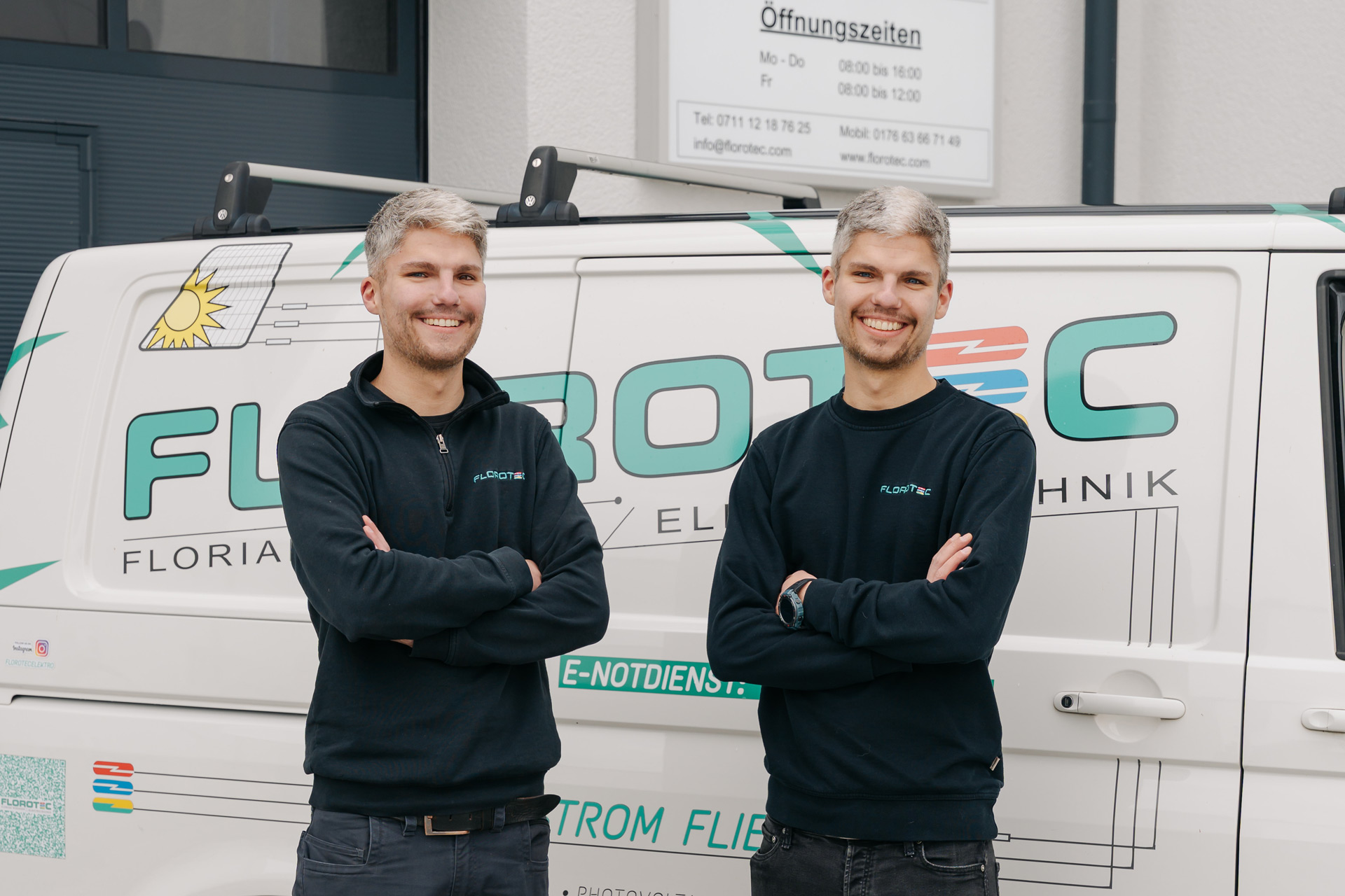 Zwei junge Männer mit kurzem blondem Haar lächeln freundlich vor einem Firmenwagen