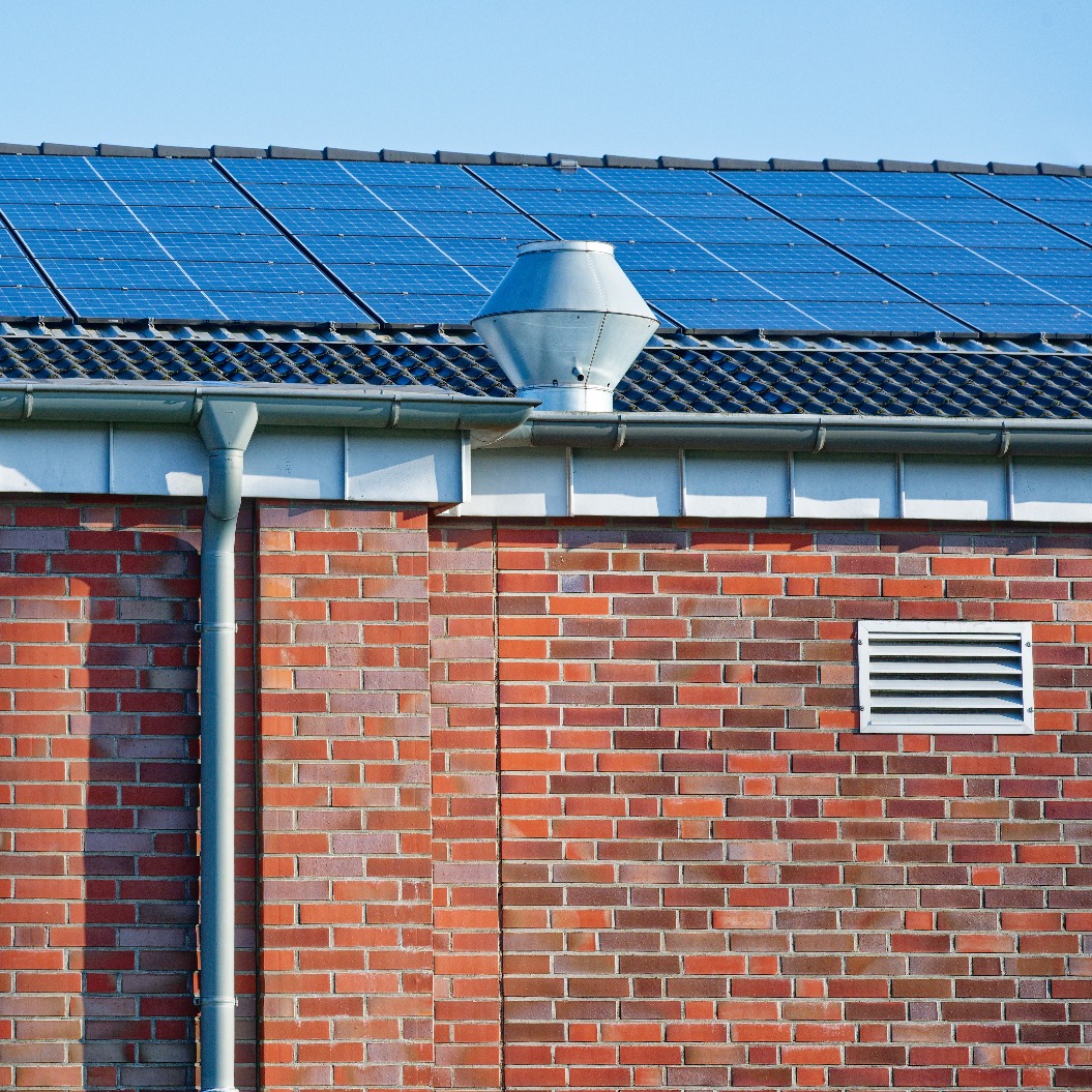 Photovoltaik-Solarmodule auf einem Dach mit einer Dachrinne aus rotem Backstein und einem industriellen Belüftungssystem
