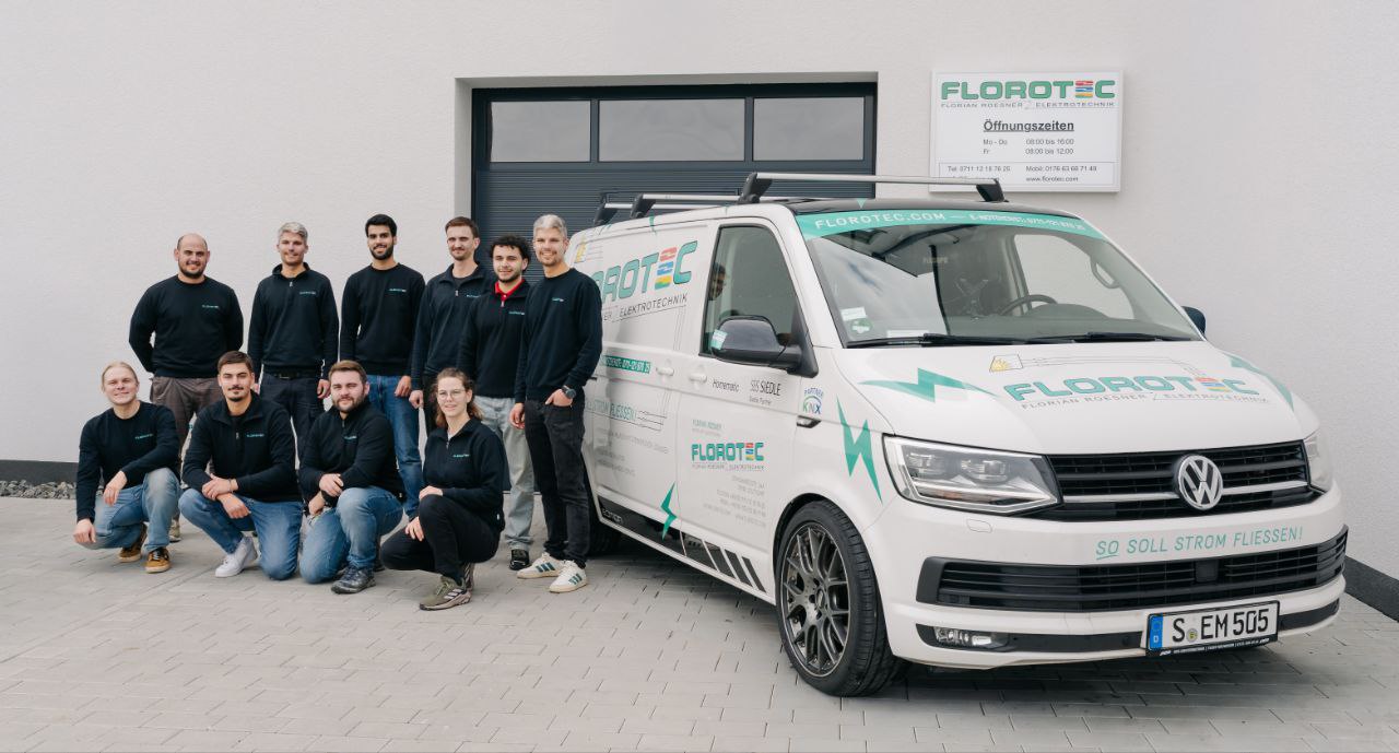 Neun Männer und zwei Frauen lächeln vor einem weißen Transporter mit Firmenlogo